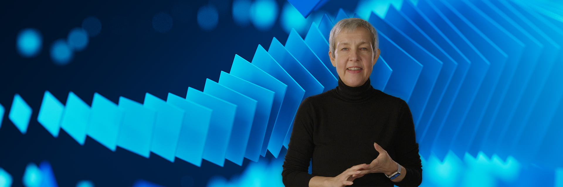 Materialise CEO Brigitte de Vet looking into the camera in front of a screen with blue squares gradually becoming larger from left to right