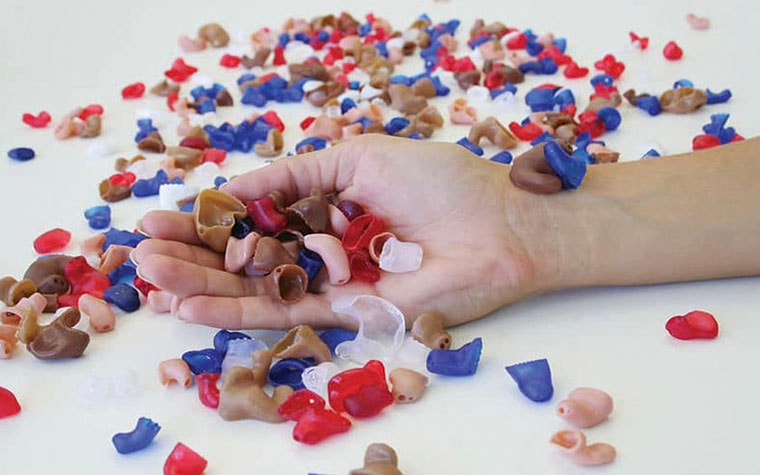 Hand holding many 3D-printed hearing aids on a table