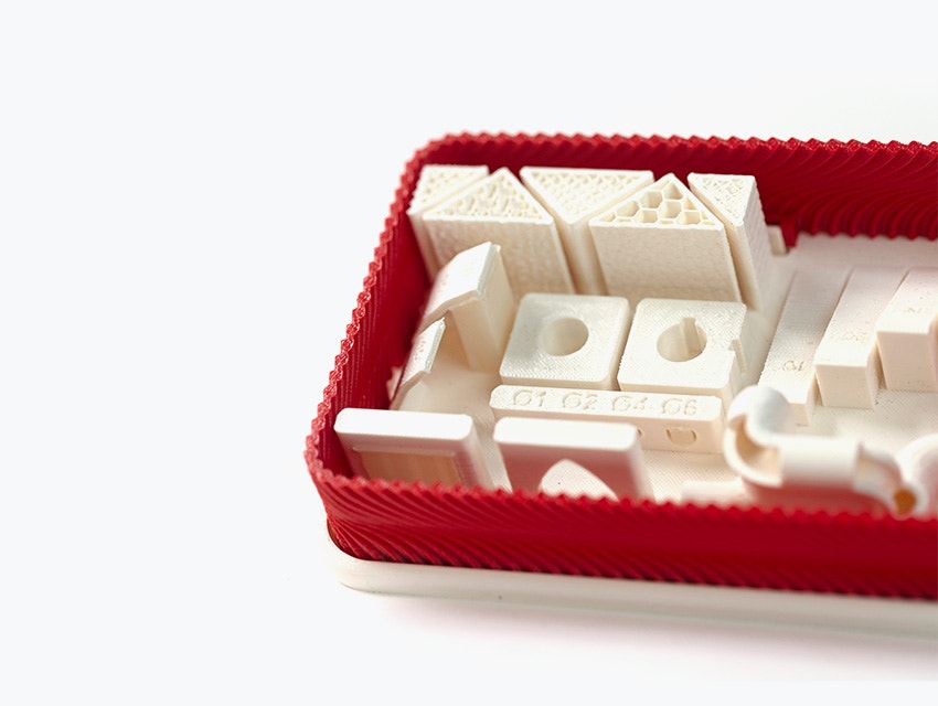 A series of white 3D-printed parts made from ABS-M30 using fused deposition modeling in a red box.