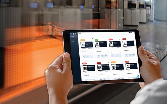 Persona che sorregge un tablet con la piattaforma software CO-AM di fronte a una stampante 3D
