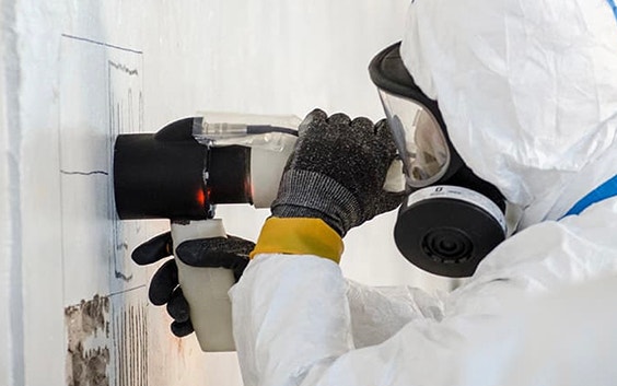 Worker wearing full personal protective equipment uses the ViridiScope to check radiation levels in a wall 