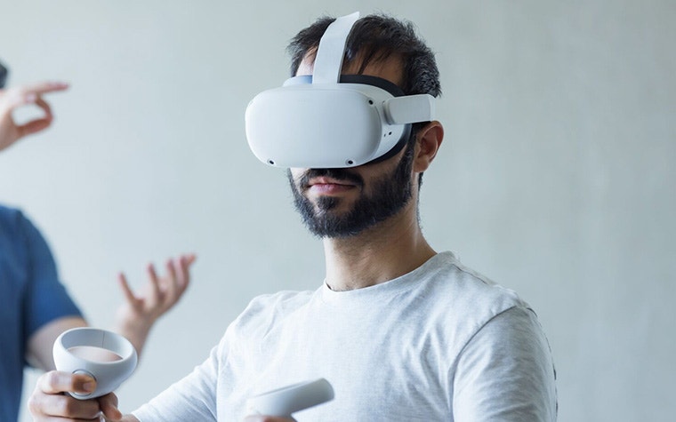 Man wearing a Meta Quest 2 VR headset while holding two remotes
