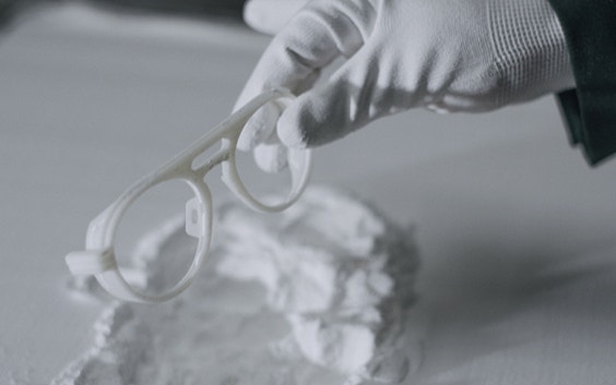 Hände mit Handschuhen entfernen 3D-gedruckte Brillengestelle von Odette Lunettes aus einem Pulverbett