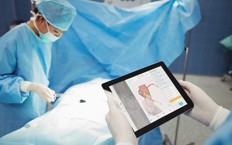 Surgeon holding a tablet in the OR and reviewing digital plan for structural heart surgery with Mimics Planner while another surgeon prepares the patient for surgery