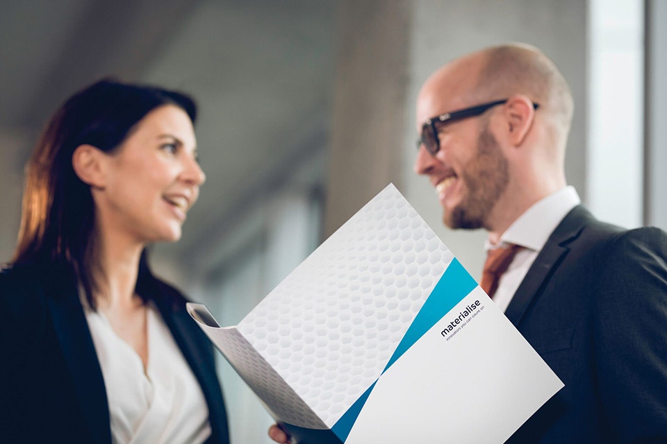 Man and woman talking and smiling while holding a Materialise folder