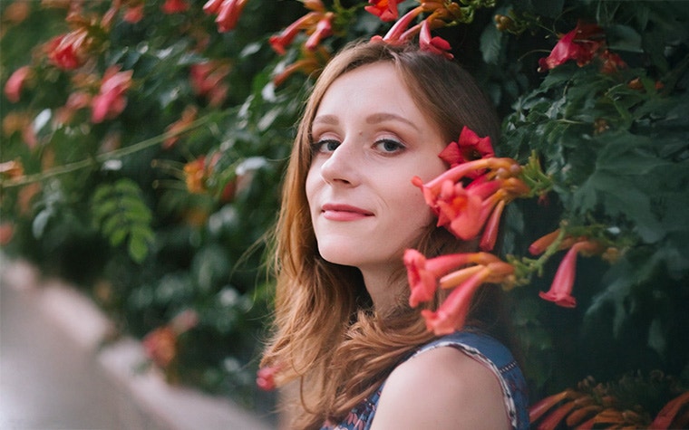 A profile picture of Olena Zhabynska. She is standing infront of a wall of red flowers.