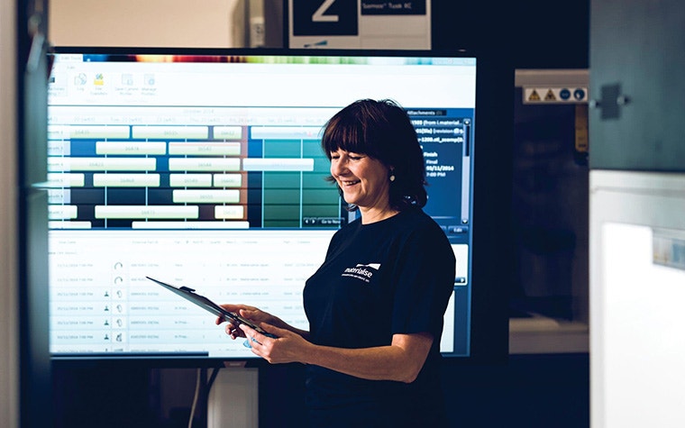 Female Materialise employee looking at a clip board in front of a large screen in production