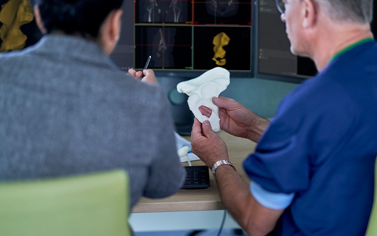 Two healthcare professionals reviewing a 3D-printed anatomical model in front of medical planning software