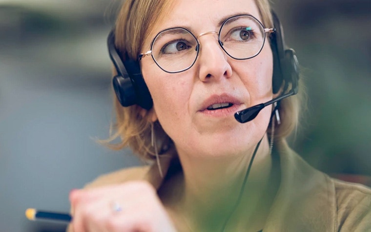 Customer support officer holding a pen while talking to a customer via a headset