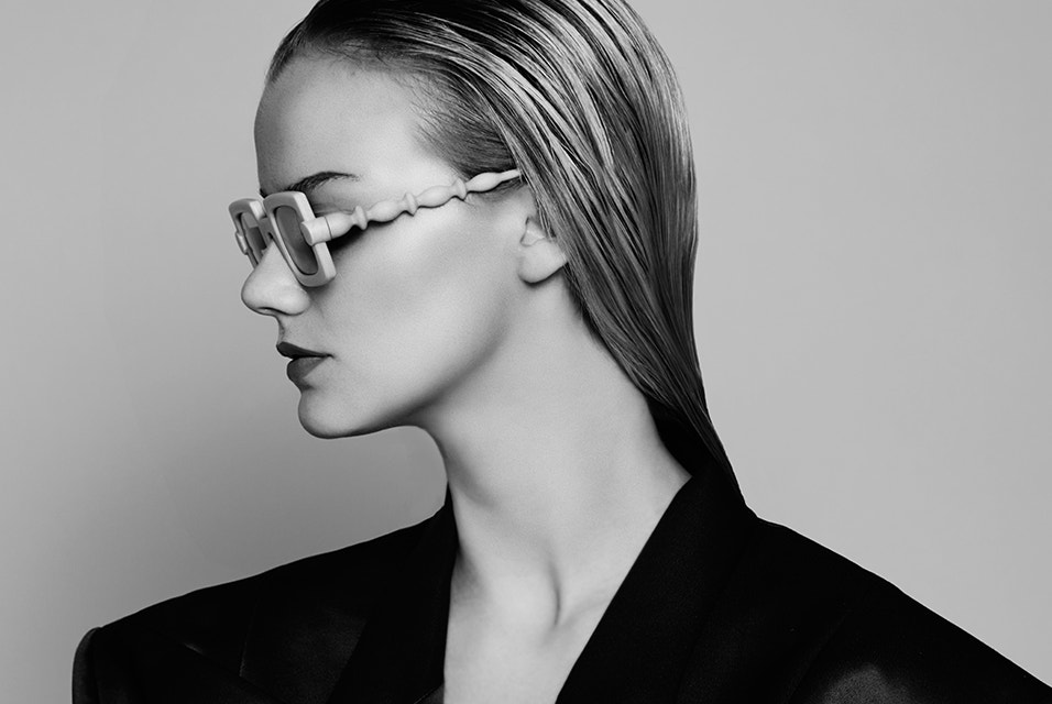 Imagen en escala de grises de una modelo peinada con el pelo hacia atrás mirando hacia un lado y que lleva gafas en color carne de BAARS x Gogosha