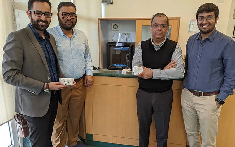 Four team members holding anatomical models in front of a 3D printer 