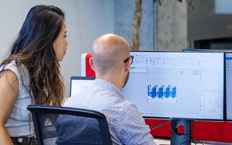 A man and woman looking at two computer screens with Materialise Nester software installed.