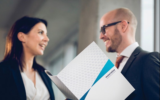 Man and woman talking and smiling while holding a Materialise folder