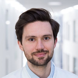 Dr.Dr. Simon Bigus wurde als Mann mit dunklem, glatt geschnittenem Haar dargestellt.