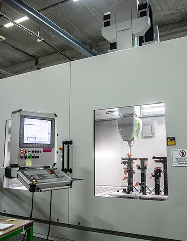 Control panel of a CNC milling machine, beside a window where the worker can see the machine at work.