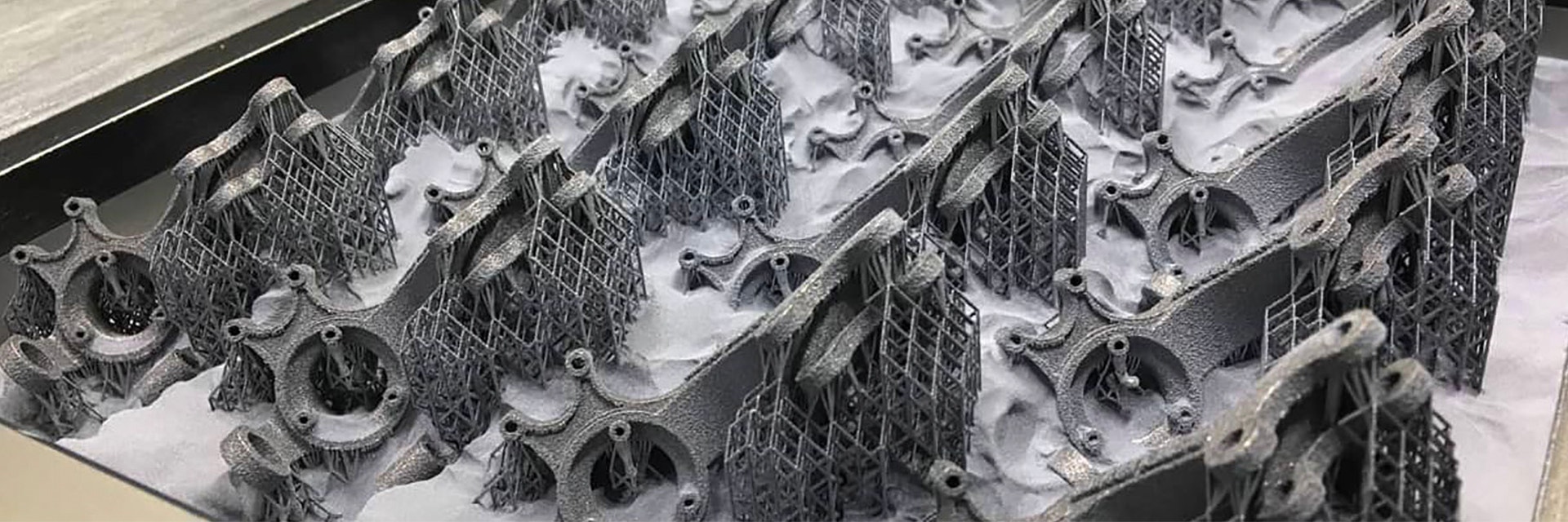 3D-printed metal parts with support structures, surrounded by loose powder