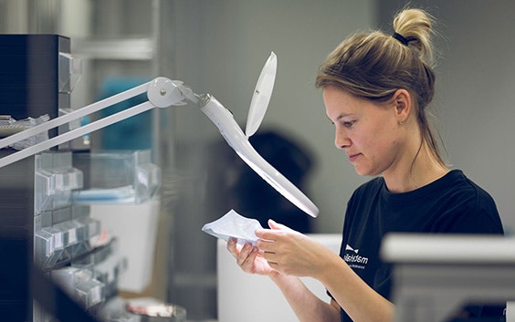 Woman inspecting a part under a magnifying glass in the Materialise production area