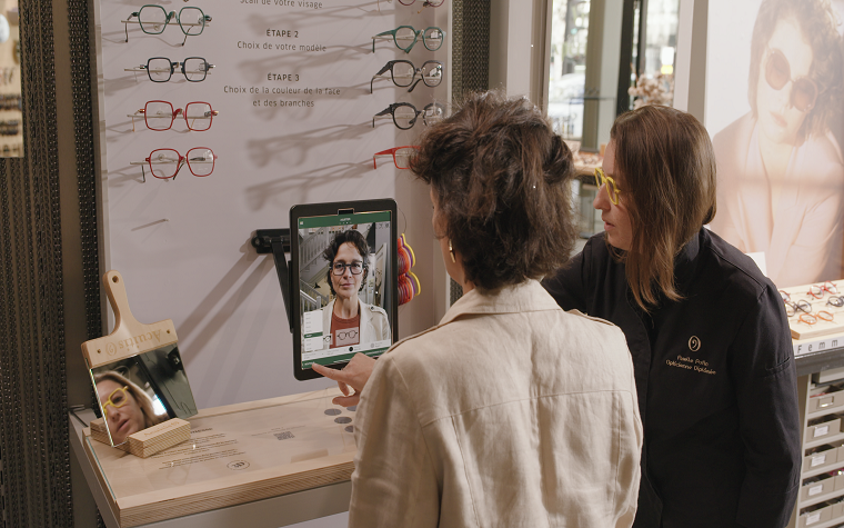 A woman explores a range of frames in the Materialise Eyewear Fitting Suite in an Acuitis store, guided by her optician.