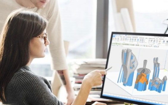 Femme assise à un bureau avec une pile de papiers, pointant avec un stylo sur un écran affichant Magics