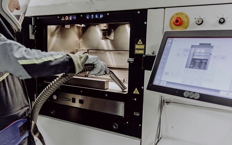 A production worker wearing a protective suit while vacuuming up metal powder from a 3D printer's powder bed