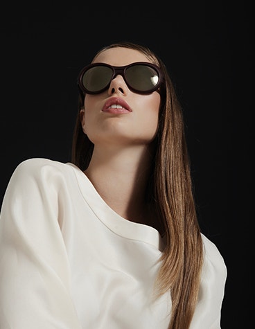 Modella vestita di bianco, guarda verso l'alto e indossa occhiali da sole neri della collezione Hoet Cabrio