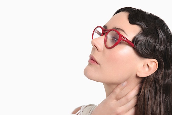 Weibliches Modell mit gewelltem Haar, das sich den Nacken hält und nach oben schaut, mit roter Yuniku-Cabrio-Brille