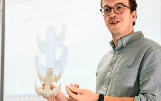 Instructor explaining a point in front of a screen while holding a 3D-printed part