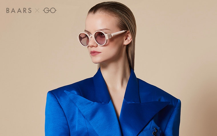 Weibliches Model in Blau, das eine nudefarbene Sonnenbrille von BAARS x Gogosha trägt und zur Seite schaut.