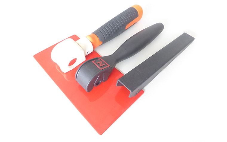A black metal cutting tool, a black plastic cutting tool, and a 3D-printed cutting tool on a red piece of metal.