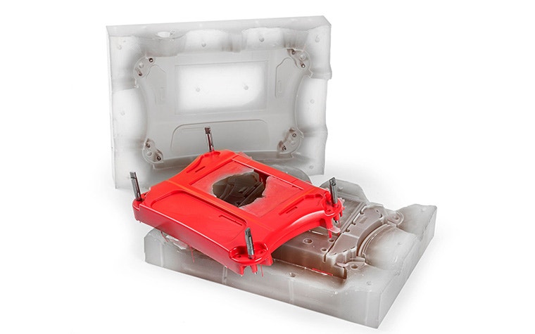 A red plastic part created using vacuum casting sitting against its silicone mold.