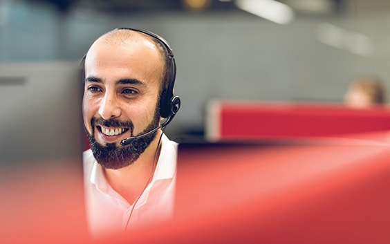 Operatore di assistenza clienti che indossa cuffie con microfono e sorride mentre osserva un computer