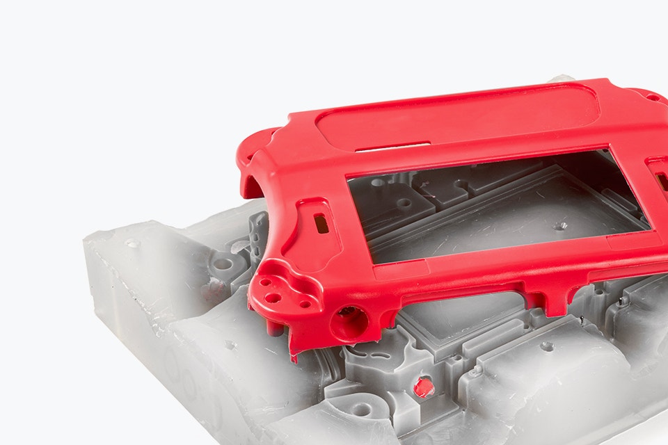 A red vacuum-cast housing on top of the silicone mold which was used to manufacture it 