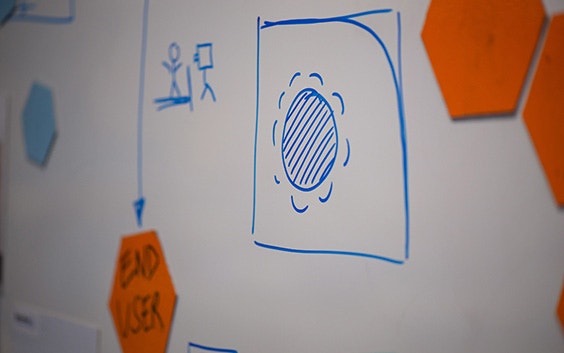 Whiteboard with stick figures and shapes drawn in blue marker and an orange piece of paper that says end user