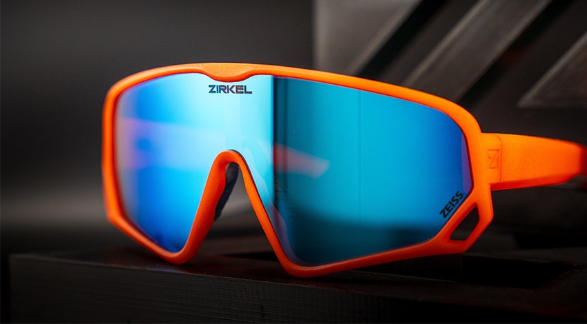 Zirkel's bright orange 3D-printed Teddy Grizz eyewear with a blue visor sitting against a dark grey and black background.