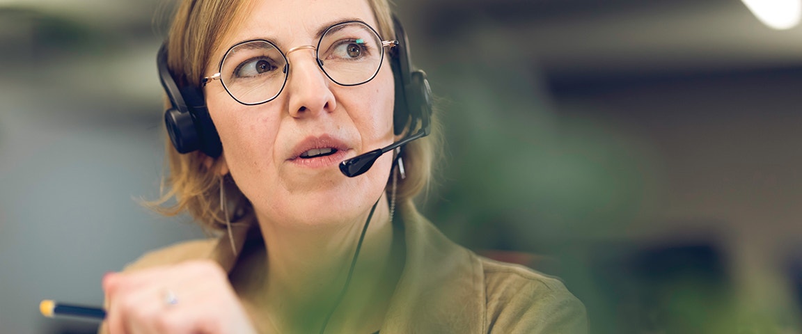 Customer support officer holding a pen while talking to a customer via a headset