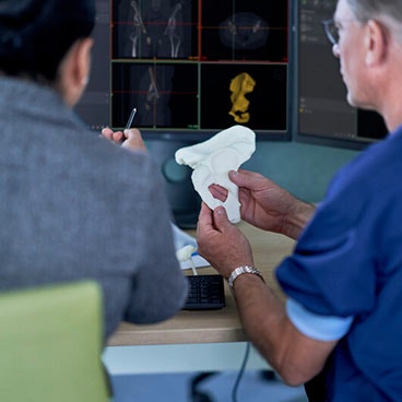 Man holding a 3D-printed hip model at a desk next to a woman pointing at 3D planning software on a computer