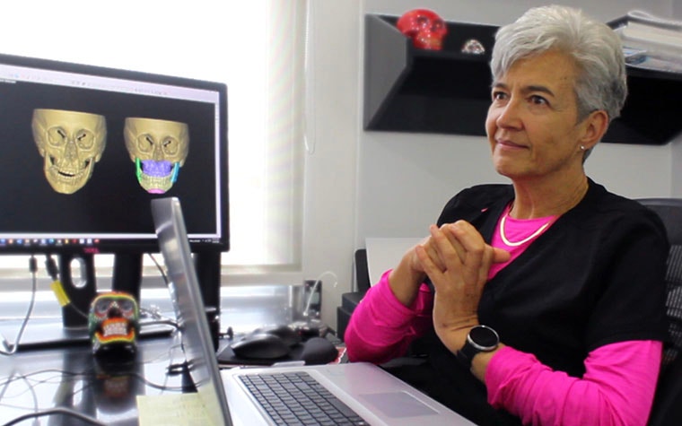 Dr. María Clara Jaramillo Campuzano sitting in front of a computer with her hands clasped