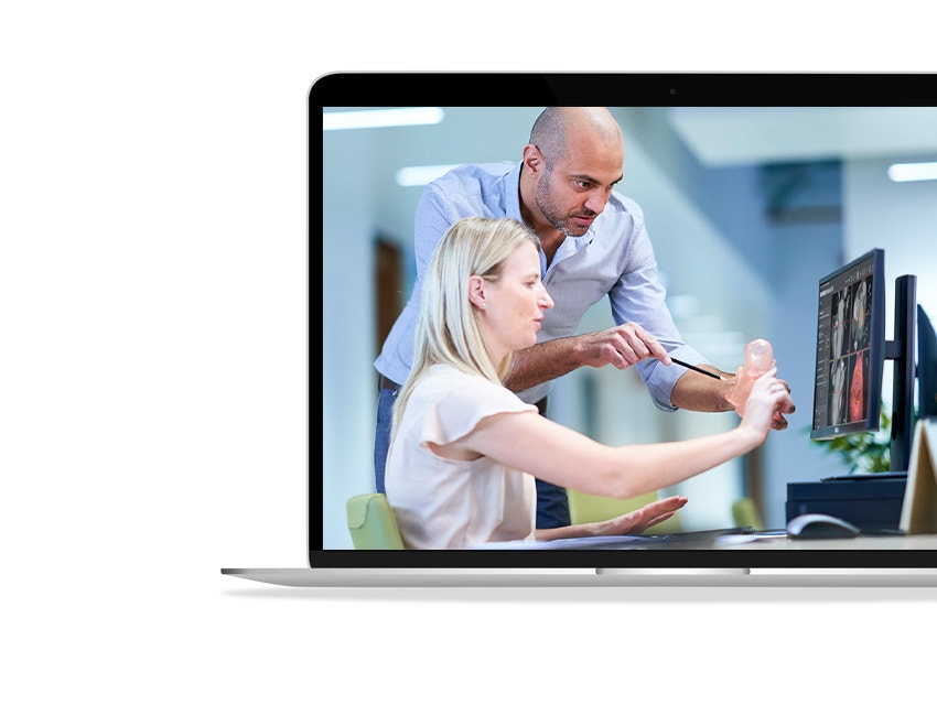 Pantalla de ordenador portátil que muestra a una mujer sentada y a un hombre de pie, ambos mirando un modelo anatómico delante de una pantalla de ordenador.