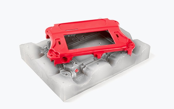 A red vacuum-cast housing on top of the silicone mold which was used to manufacture it 