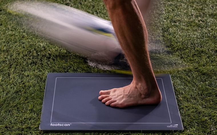 A barefooted player striking a soccer ball while on a pressure plate