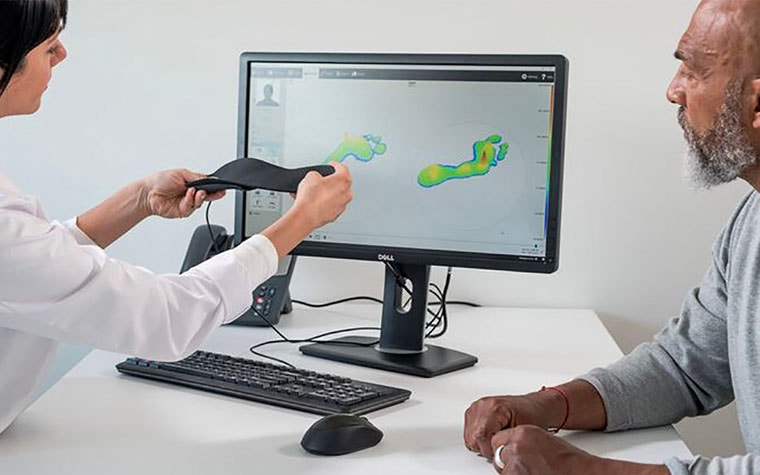 Podiatrist explaining the custom 3D-printed insole to her patient in front of a computer screen
