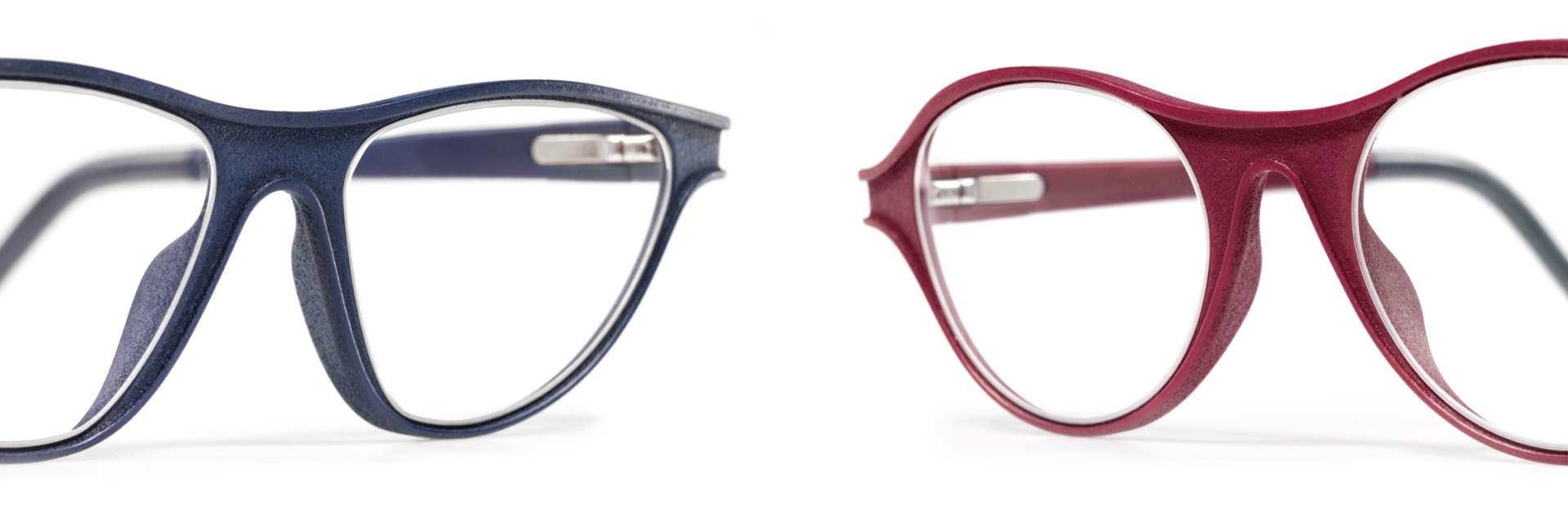 Dos pares de monturas de gafas impresas en 3D con acabado Luxura, una en azul vaquero y otra en rojo frambuesa
