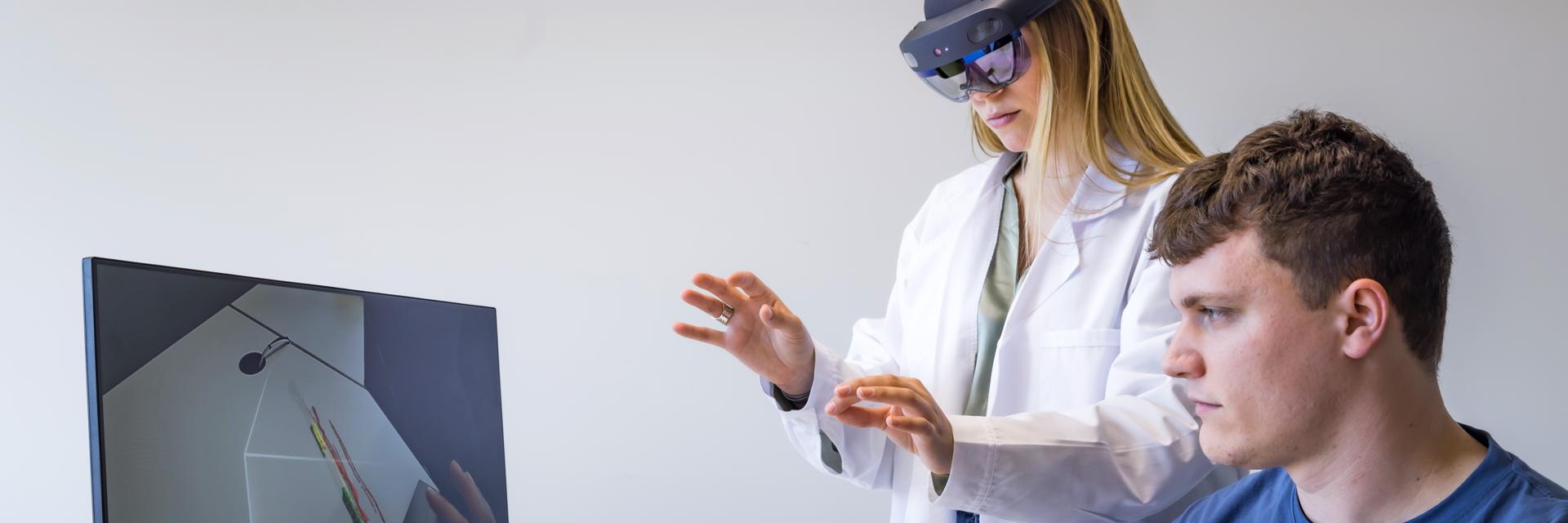A doctor wearing AR goggles while virtually adjusting measurements while a man watches the process on a monitor