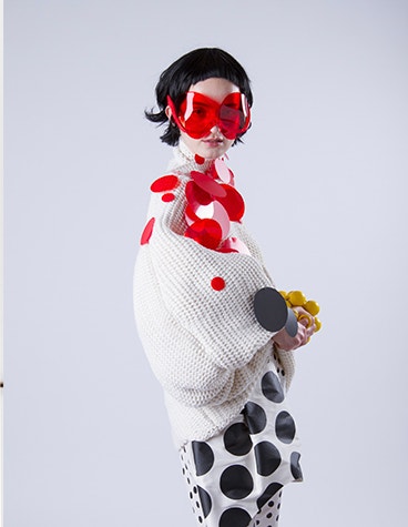 Model in einem weißen Outfit mit roten und schwarzen Kreisen und einer roten Sonnenbrille, entworfen von David Ring