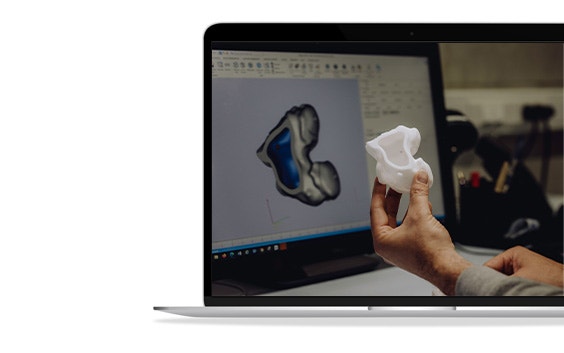 A hand holding up a 3D-printed anatomical model in front of a laptop screen with Mimics open.