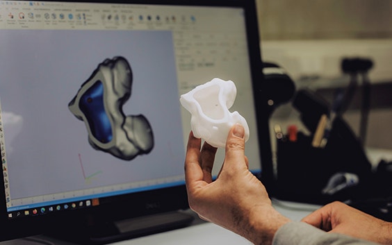 Mano sosteniendo un modelo anatómico impreso en 3D frente a un diseño en 3D en un ordenador