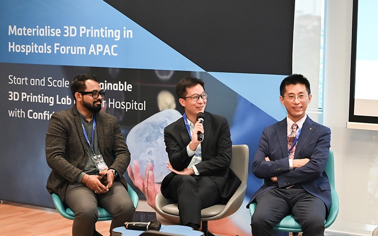 A group of 3 men sitting in chairs at the conference.