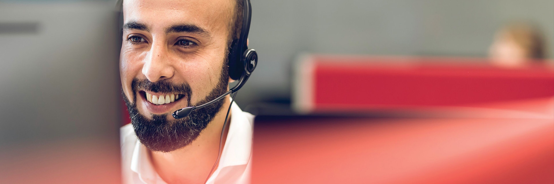 Customer support officer smiling while looking at a computer and wearing a headset