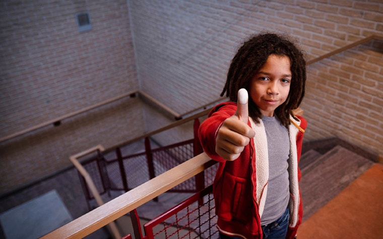 Child posing in a stairway, giving a thumbs up with white paint on the thumb