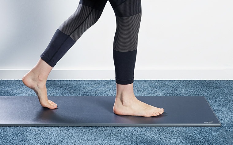 A barefoot woman walking on the Materialise Footscan Pro Level pressure plate in a room with blue carpet.